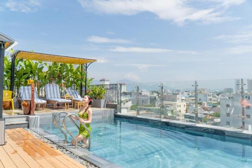 a woman sitting on the edge of a swimming pool on top of a hotel at Seahorse Signature Danang Hotel by Haviland in Da Nang