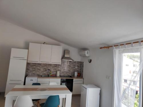 a kitchen with white cabinets and a table and a window at Apartments Radić in Rogoznica