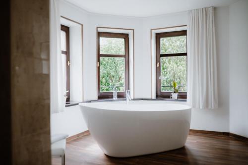 a large white tub in a bathroom with windows at Schlosshotel Stecklenberg in Thale