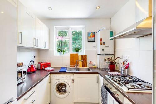 cocina con armarios blancos, lavadora y secadora en Modernistic 2 BR maisonette in Kingsbury en Colindale