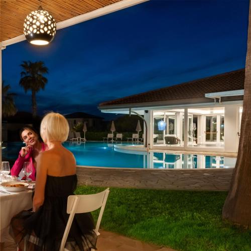 a woman sitting at a table in front of a pool at Paestum Inn Beach Resort in Paestum