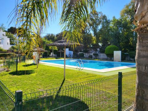 una piscina con una palmera y una valla en Casa Playa La Fontanilla SOTOLODGE en Conil de la Frontera
