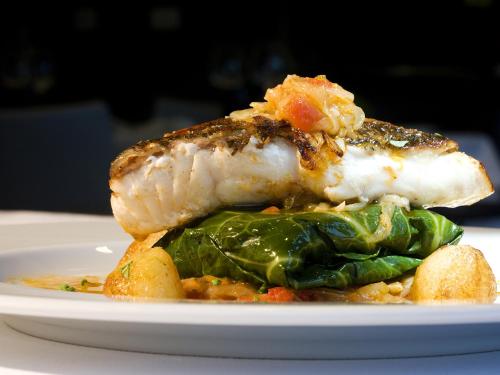 a piece of fish on a white plate with greens at Melia Braga Hotel & Spa in Braga
