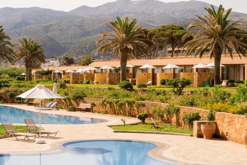 a resort with a pool and palm trees and mountains at Kernos Beach Hotel & Bungalows in Malia