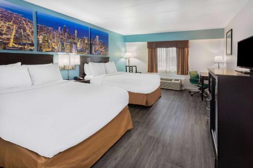 a hotel room with two beds and a flat screen tv at Days Inn by Wyndham Livonia Canton Detroit in Livonia