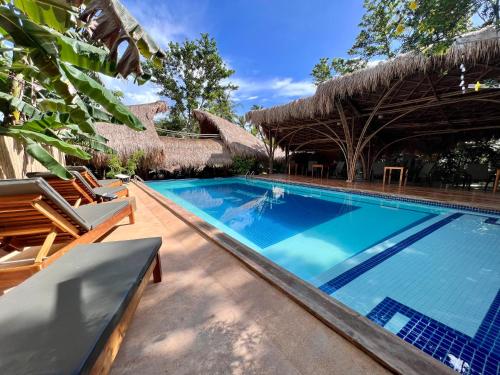 a swimming pool at a resort with chairs and a thatch roof at La Colonial Resort in El Nido