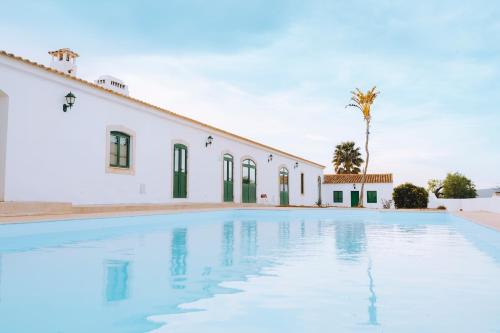 a swimming pool in front of a white building at Cerca Velha - Country House in Albufeira