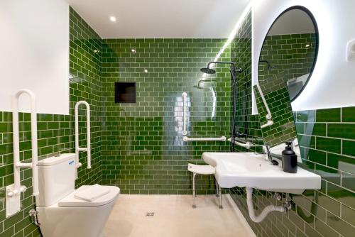 uma casa de banho com azulejos verdes, um WC e um lavatório. em Stayaday Apartments Albufera em Madri