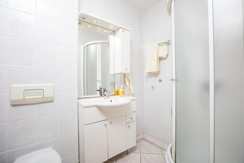 La salle de bains blanche est pourvue d'un lavabo et d'une douche. dans l'établissement Apartments Barjaktarić, à Malinska