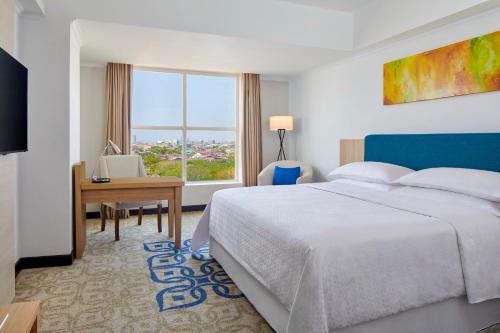 a bedroom with a bed and a desk and a window at Four Points by Sheraton Makassar in Makassar