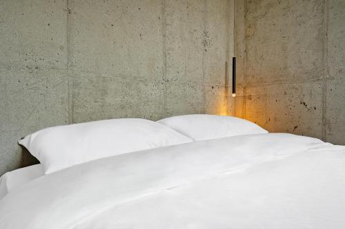 a bedroom with a white bed with a concrete wall at Ingu Stay in Yangyang