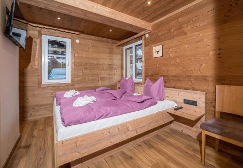 Bett in einem Blockhaus mit lila Daunendecke in der Unterkunft Schima Drosa Apartments - Studios - by Pferd auf Wolke in Gaschurn