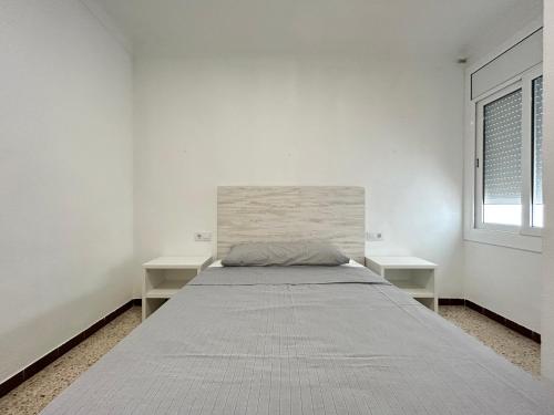 een bed in een witte kamer met 2 tafels bij Apartamentos playa la Perola in Roses