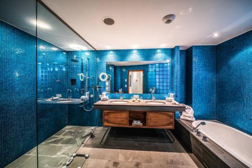 y baño con paredes de azulejos azules, bañera y lavamanos. en Hotel Krallerhof, en Leogang