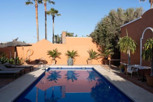 a swimming pool with palm trees and a building at Hotel Madreselva - Grupo Califa in Los Caños de Meca