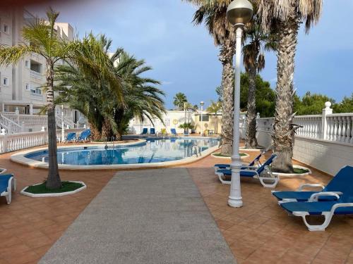 uma piscina com palmeiras e espreguiçadeiras azuis em Cozy Apartment in Guardamar em Guardamar del Segura