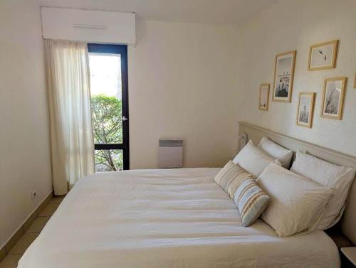 un grand lit blanc dans une chambre avec une fenêtre dans l'établissement T3 clim piscine chauffée proche de la plage parking dans village vacances, au Cap d'Agde