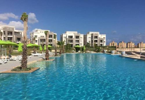 a large swimming pool with palm trees and buildings at شاليه بقرية امواج الساحل الشمالي 3 غرفة Amwaj North Coast in El Alamein