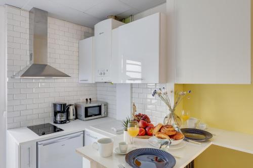 kuchnia z białymi szafkami i miską owoców na ladzie w obiekcie Modern Stylish and Chic Apartment next to the Famous Paris Catacombs w Paryżu