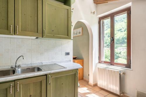 cocina con armarios verdes, fregadero y ventana en * Villa Ulivi - Private Pool with Panoramic Views en Barga