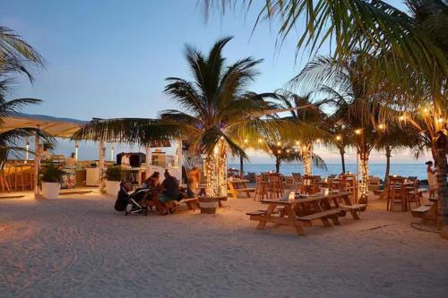 un gruppo di persone seduti su una spiaggia con tavoli e palme di Vibrant Studio Near the Beach a Jan Thiel