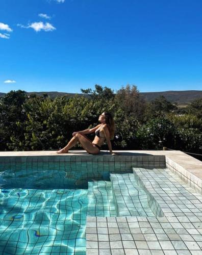 a woman in a bikini sitting next to a swimming pool at Statera Host in Alto Paraíso de Goiás