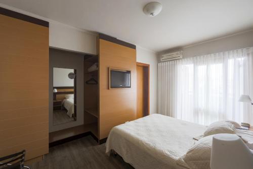 1 dormitorio con cama, espejo y TV en Flat Avenida Independência en Porto Alegre