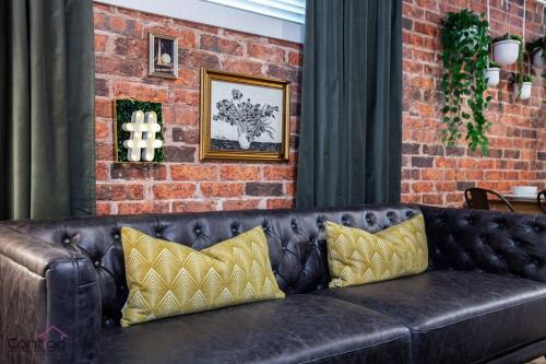 a black leather couch with yellow pillows next to a brick wall at Luxe New York Style Bsmt Suite, Near DT & WEM, King Bed, WiFi in Edmonton