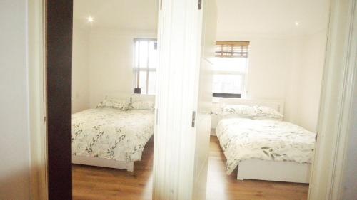 a white bedroom with two beds and a window at London Apartments 4U in London