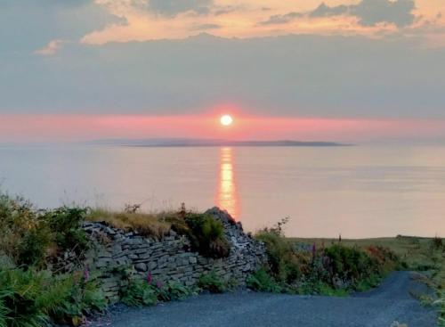 a sunset over the water with a stone wall at Blue Haven Lodge in Doolin