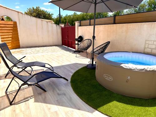 patio con vasca idromassaggio, sedie e ombrellone di Maison de charme avec Jacuzzi a Mollégès