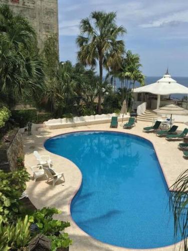 a large blue swimming pool with chairs and umbrellas at Villa Palmitas acogedor departamento nivel piscina gigante jardines in Acapulco