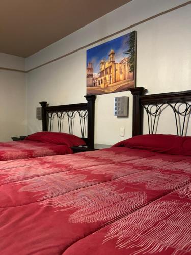 THIZMA HOTELES Ex HotelSantaMaria في اياكوتشو: غرفة نوم بسريرين مع شراشف حمراء ولوحة