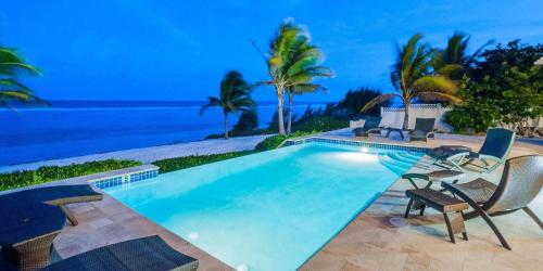 a swimming pool with chairs and the ocean in the background at In Harmony by Grand Cayman Villas & Condos in Bodden Town