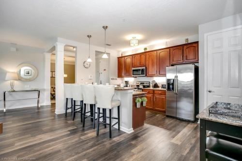 a kitchen with wooden cabinets and a bar with white bar stools at Lake View 3 Bedroom In Vista Cay Resort condo in Orlando