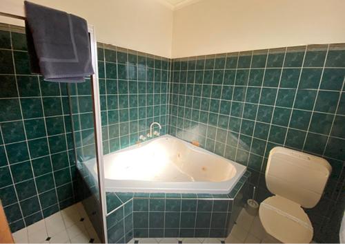 baño de azulejos verdes con bañera y aseo en Railway Hotel Motel Peterborough, en Peterborough
