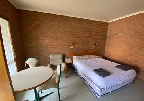 a bedroom with a bed and a table and a brick wall at Railway Hotel Motel Peterborough in Peterborough