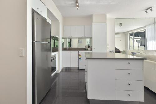 una cucina con armadi bianchi e frigorifero in acciaio inossidabile di The Cove Noosa - Apartment 20 a Noosa Heads