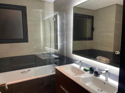 een badkamer met een wastafel, een spiegel en een bad bij Blue Apartment vue sur l’océan : Taghazout bay in Taghazout