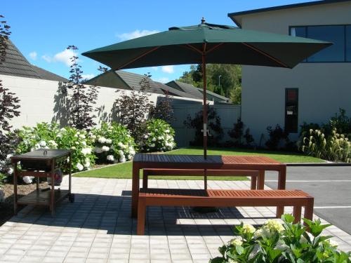 een picknicktafel met een parasol en een grill bij Alpine Lake Motel in Taupo