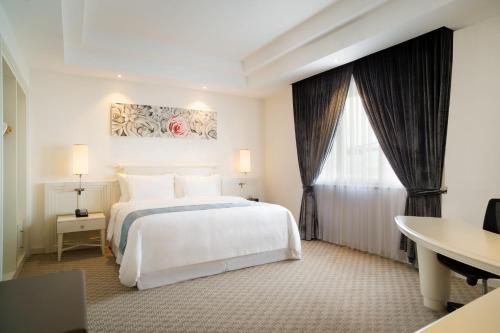 a bedroom with a white bed and a desk and a window at Four Points by Sheraton Bandung in Bandung