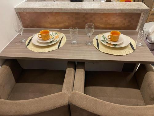 a table with two cups and plates and glasses at Flat Hotel Samba Barra Jeunesse Arena Projac Rio Centro in Rio de Janeiro