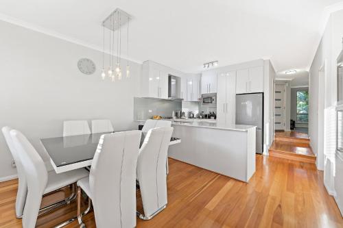a white kitchen with a dining table and white chairs at Modern Scarborough Townhouse in Perth