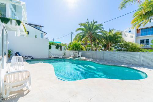 a swimming pool with two chairs and a white house at Beach Palms Holiday Apartments in Gold Coast