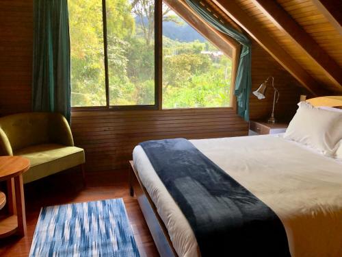 ein Schlafzimmer mit einem Bett, einem Fenster und einem Stuhl in der Unterkunft Zafiro Boutique Hotel in Mindo