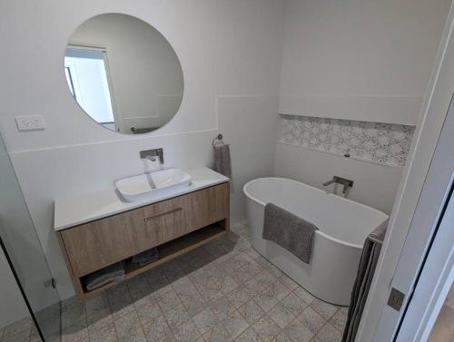een badkamer met een wastafel, een bad en een spiegel bij Bateau Bay Retreat in Bateau Bay
