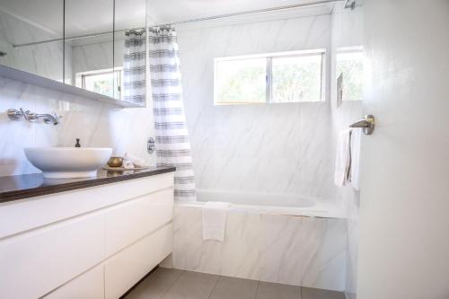 a white bathroom with a tub and a sink at Mid-Century Modern Retro Beach House in Caloundra