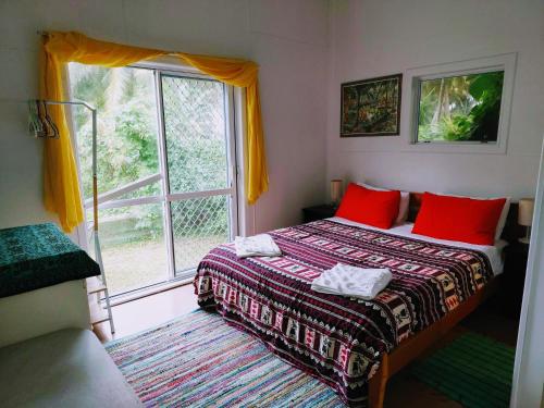 a bedroom with a bed with red pillows and a window at Barefoot Base Tupapa in Rarotonga