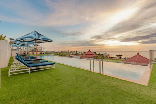 a pool with chairs and an umbrella on the grass at Holiday Inn Express Baruna by IHG in Kuta