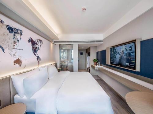 a bedroom with a large white bed and a world map on the wall at Kyriad Marvelous Hotel Qinhuangdao Nandaihe in Qinhuangdao